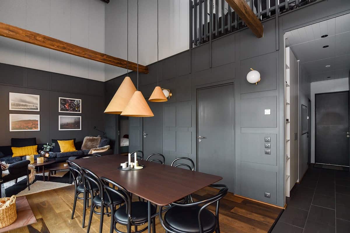 Des chaises bistrot noires autour d&rsquo;une longue table sous des suspensions en bois
